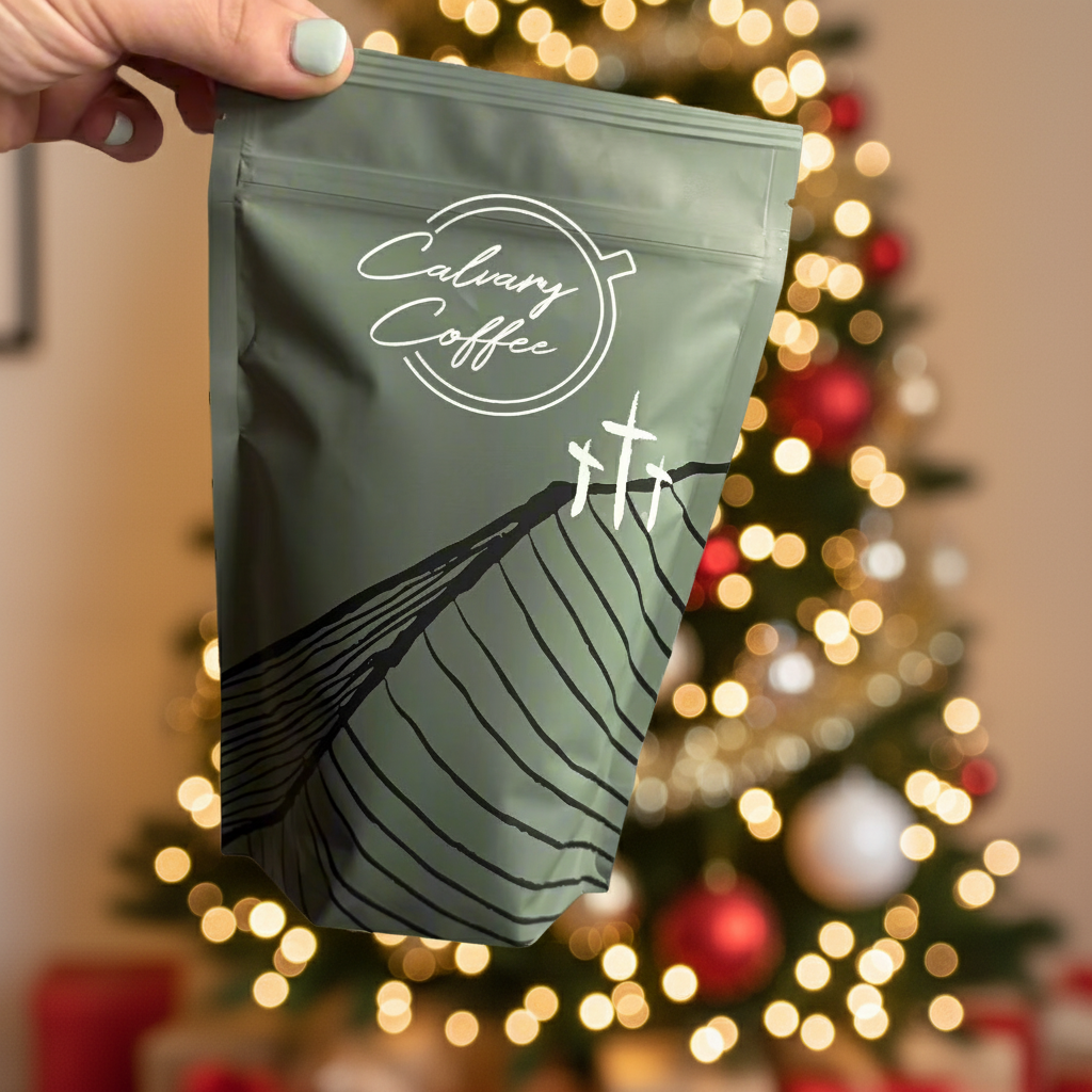 Handing holding Calvary Coffee bag in front of a Christmas tree.