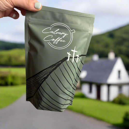 Handing holding Calvary Coffee bag in front of Irish landscape.